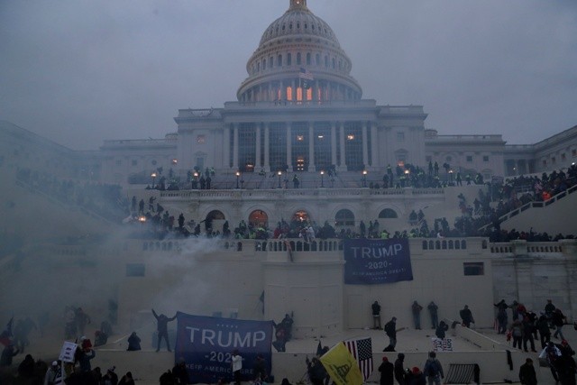 Image of the US Capitol building with tear gas and trump supporters in front of it.