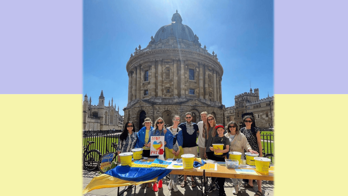 Members of the Oxford University Ukrainian Society in front of the Rad Cam on a sunny day. They are behind a table with Ukrainian flags and donations buckets.