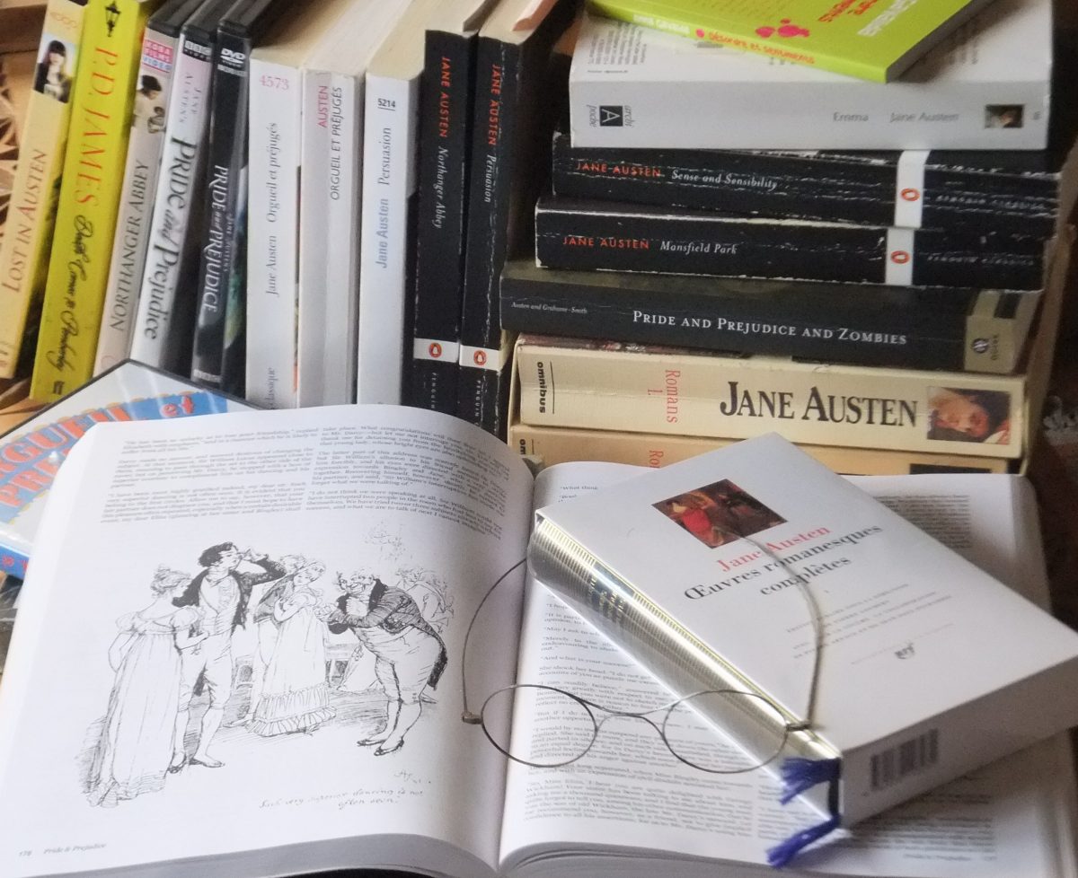 A Jane Austen novel is open on a table, with a pile of Austen novels in the background