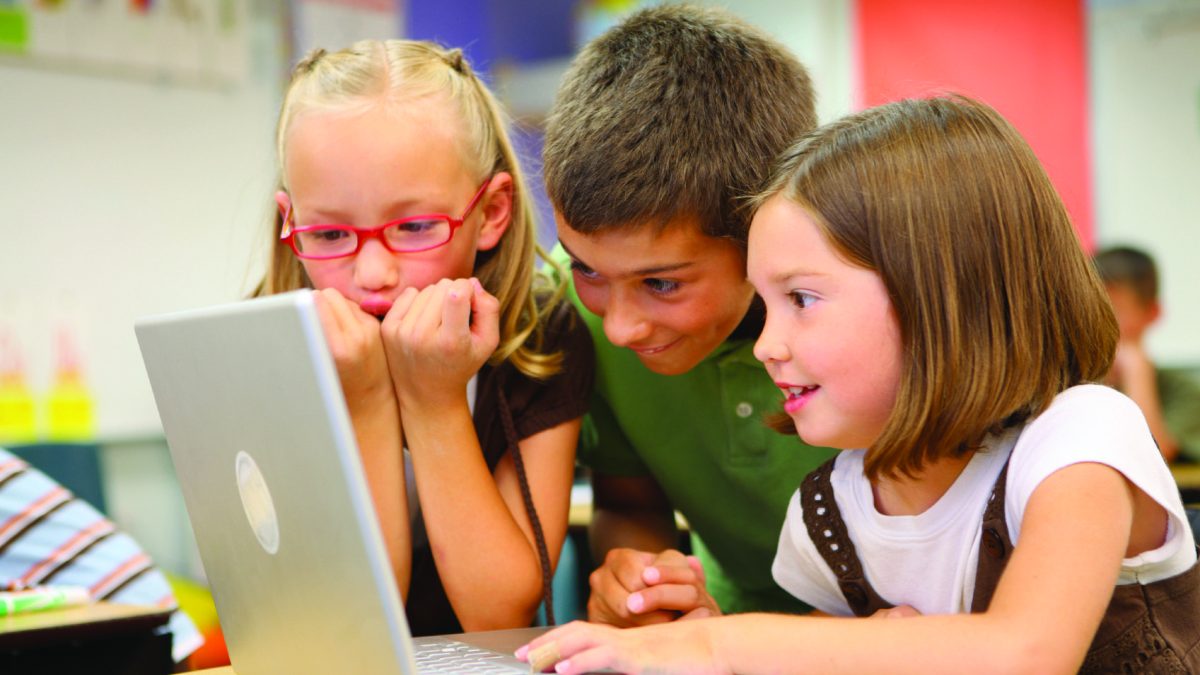 Three children look excitedly at a computer screen.