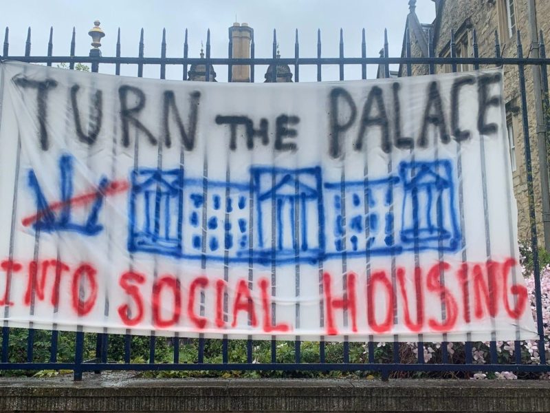 Photo of a banner reading "Turn the Palace into Social Housing" attached to Trinity College.
