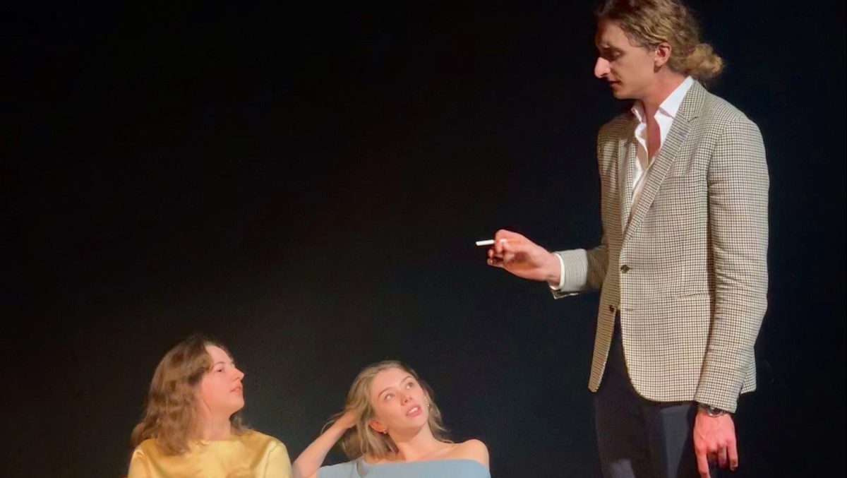 Photo of the performance in which a man in a suit looks down on two women who are sitting down