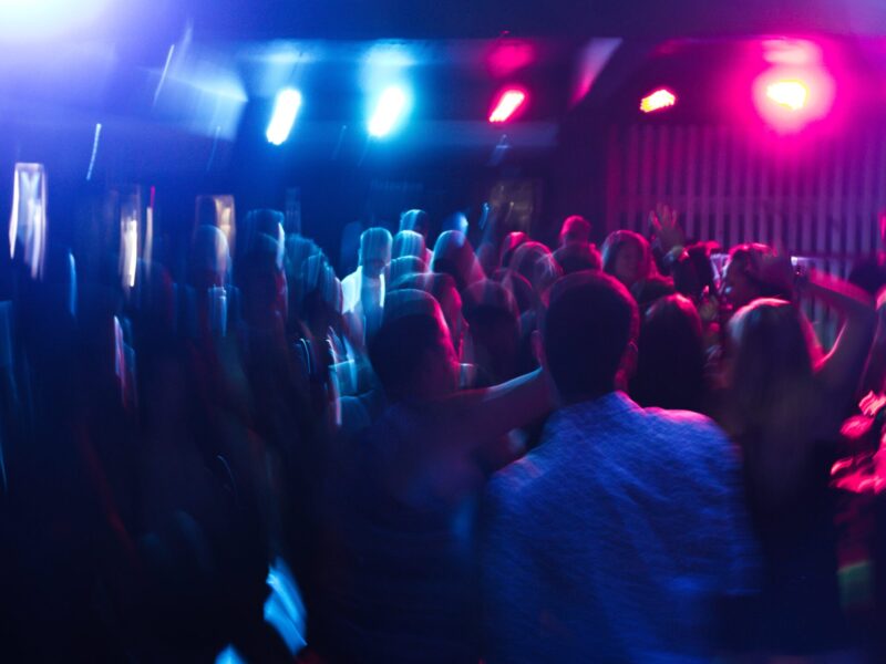 A blurry picture of young people dancing in a dark nightclub, similar to Atik, somewhat lit by a few neon lights.