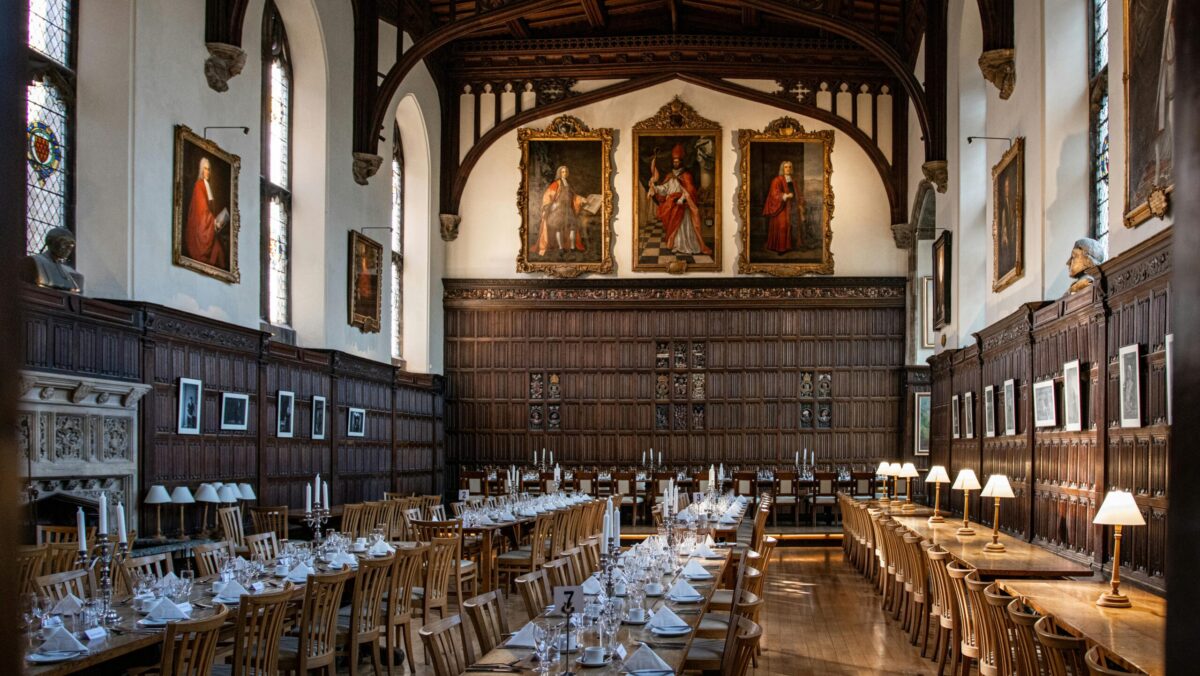 Magdalen College dining Hall, a large Oxford hall with wood panels and portraits on the walls, set for dinner.