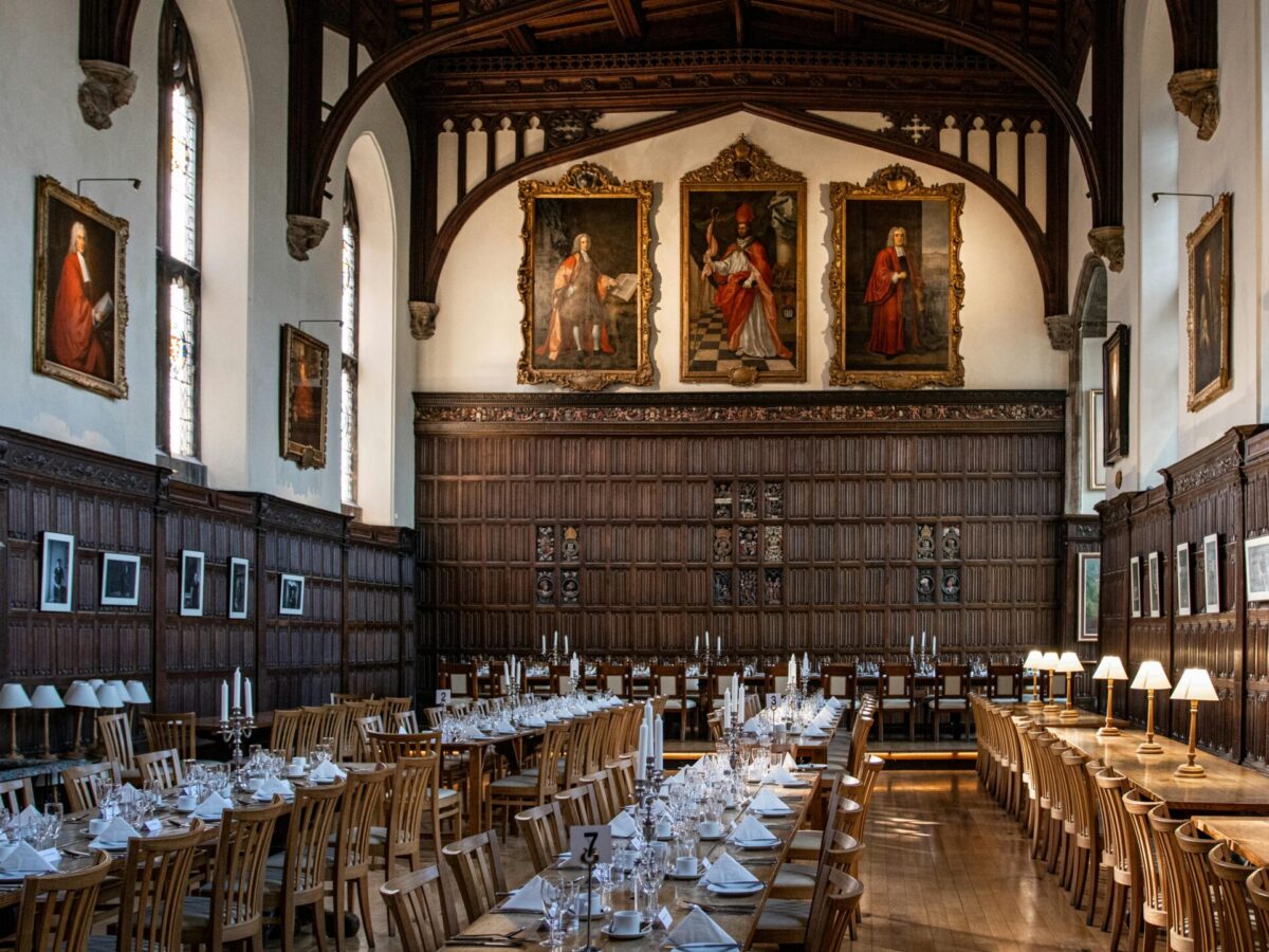 Magdalen College dining Hall, a large Oxford hall with wood panels and portraits on the walls, set for dinner.