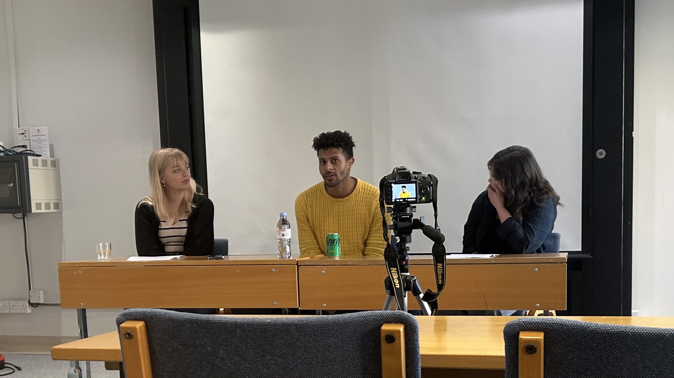 A panel with three individuals sat in a classroom.