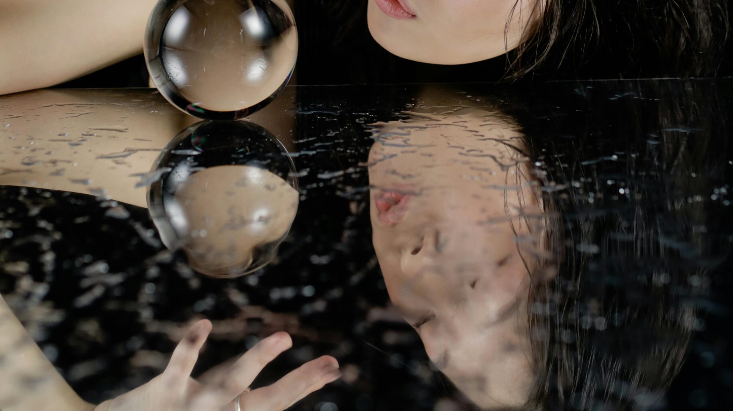 Photo shows watery reflection of a young woman's face, against a black background.