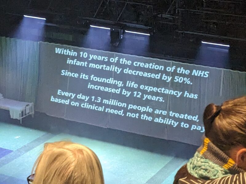 Screen at the theatre reads: within 10 years of the creation of the NHS infant mortality decreased by 50%