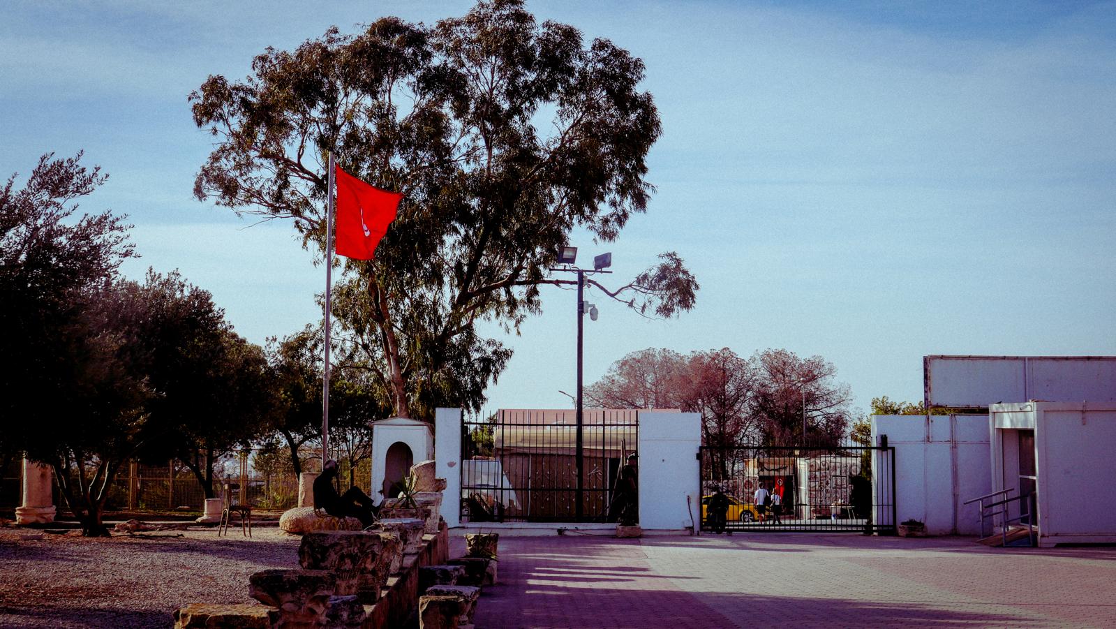 A landscape featuring white gates, a tree and red flag.