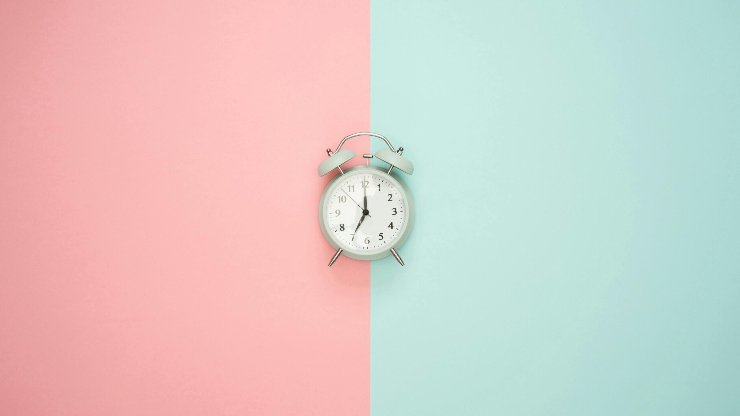 Photo of a clock on a background of pink and turquoise.