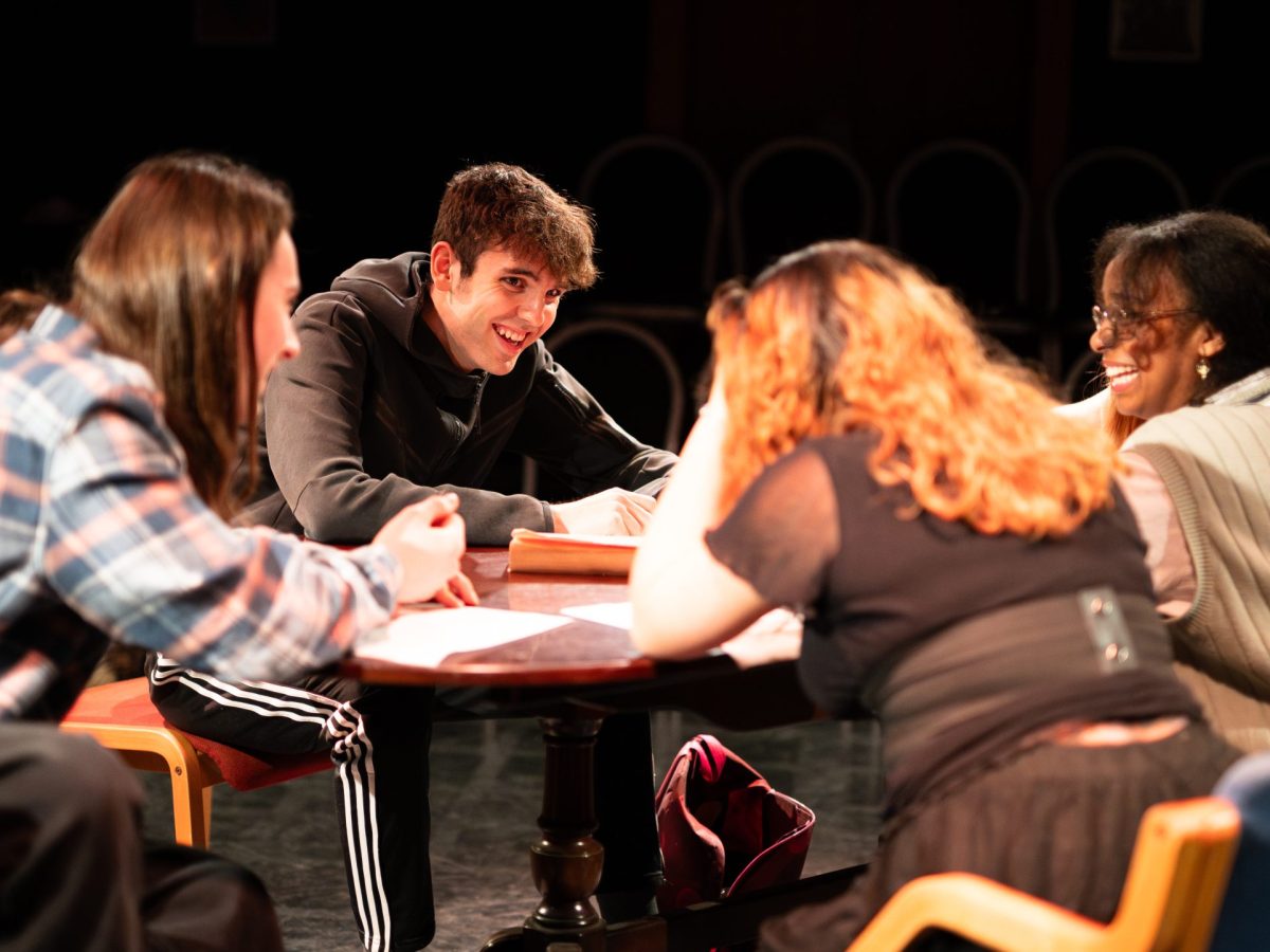 An image of four cast members sat and laughing around a table of the set