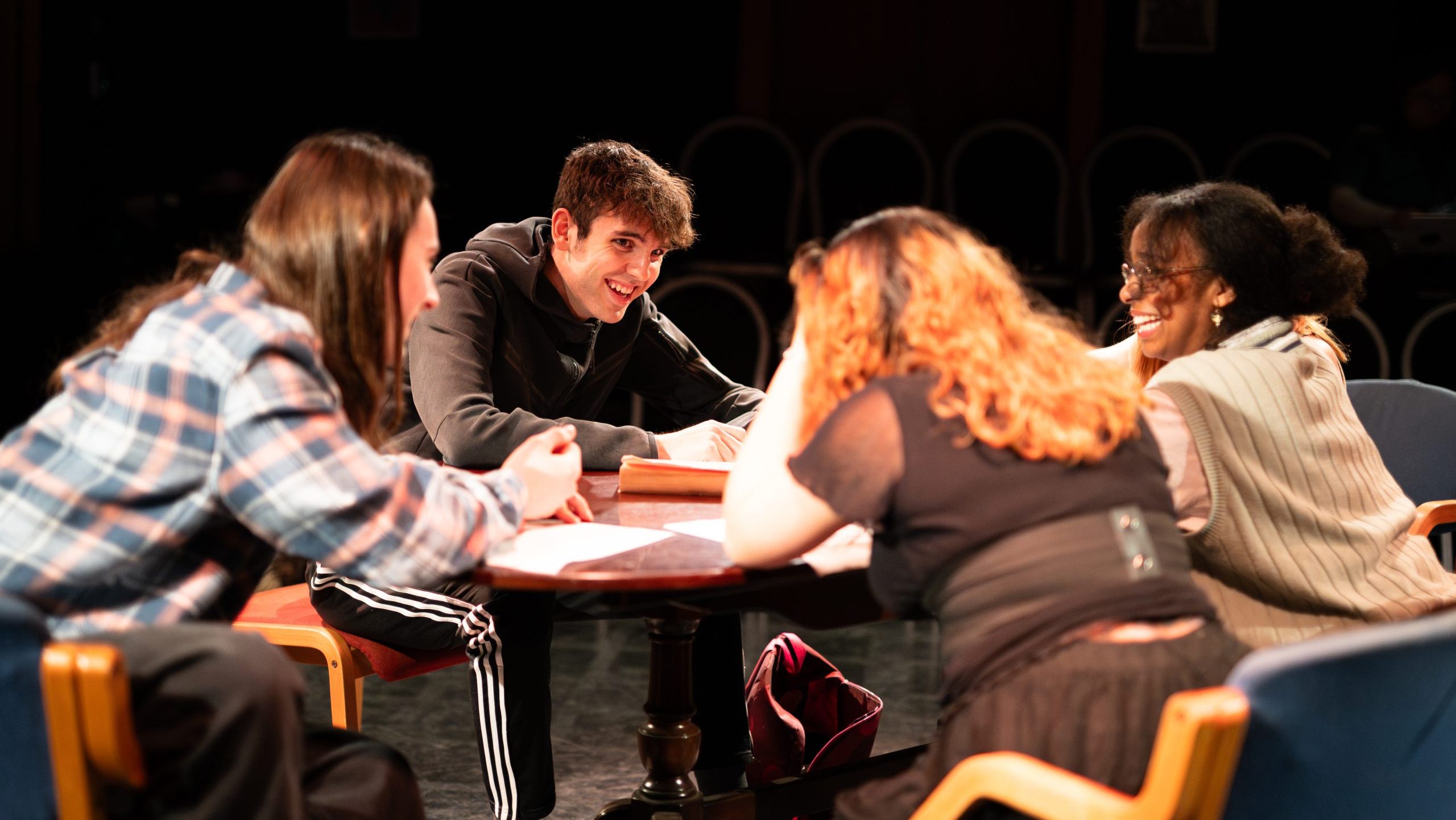 An image of four cast members sat and laughing around a table of the set