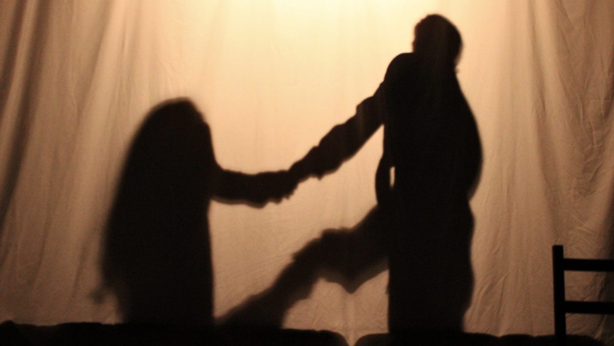 The silhouettes of a couple holding hands behind a white sheet