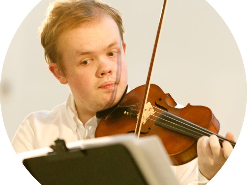 Image depicts Samuel Oliver-Sherry holding a violin and looking at sheet music on a music stand