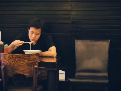 A man sits at a table alone, eating a bowl of ramen.
