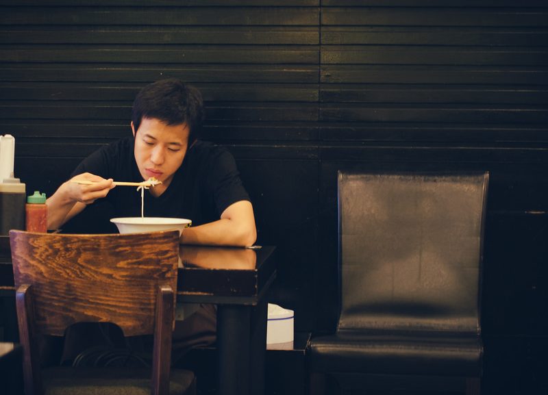 A man sits at a table alone, eating a bowl of ramen.