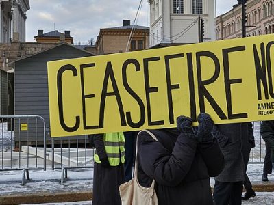 Person holds up yellow sign on which is written 'CEASEFIRE NOW Amnesty International'.
