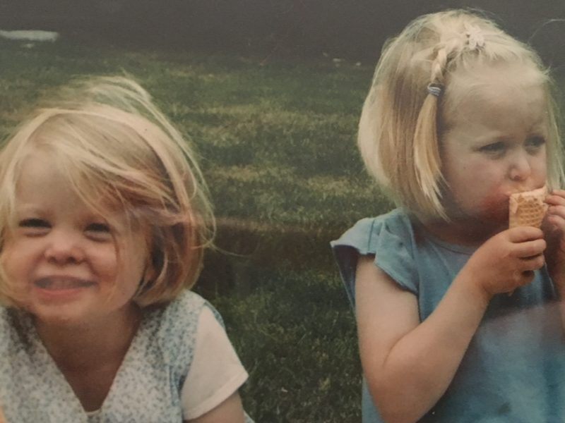 Two young sisters eating ice cream in a field.
