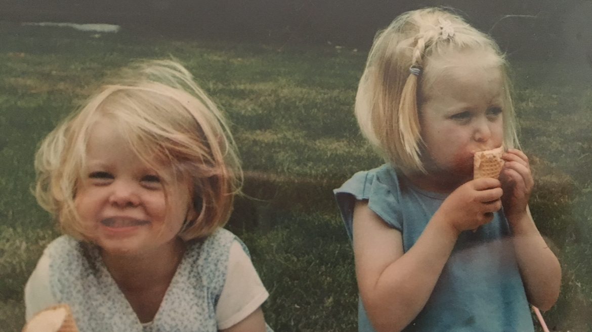 Two young sisters eating ice cream in a field.