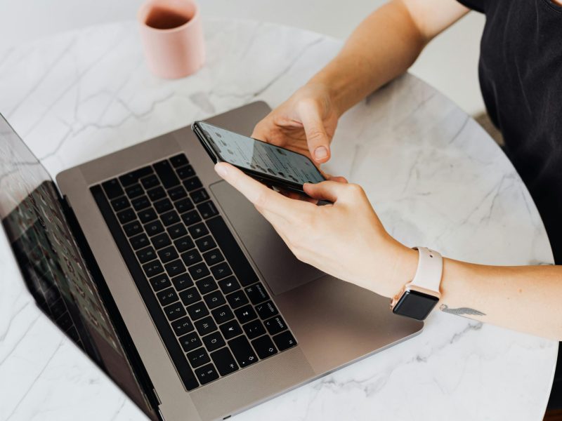 Photo of a woman using a phone and a laptop.