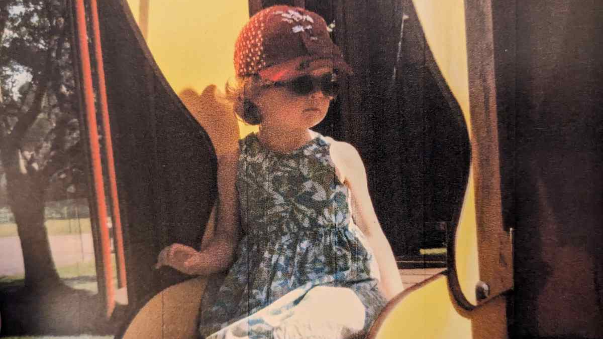 Infant sits on a slide, looking off to the side.