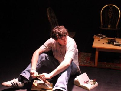 A man sits on the floor surrounded by books.