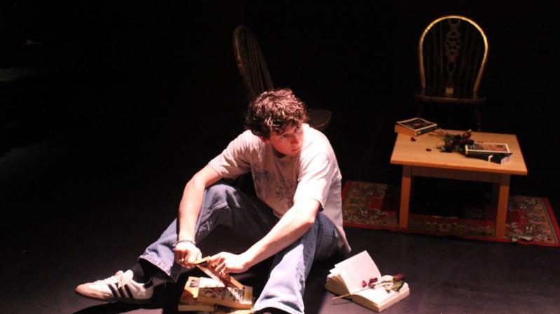 A man sits on the floor surrounded by books.
