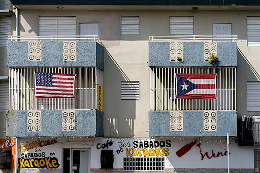 Two adjacent balconies, one bearing the flag of the United States, to other bearing the flag of Puerto Rico.