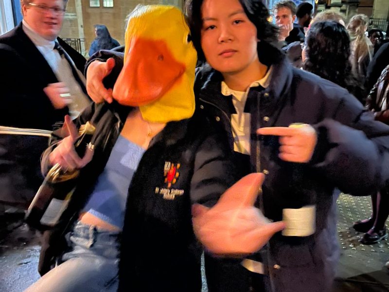 Two students at a cast party, one of them wearing a rubber duck head.
