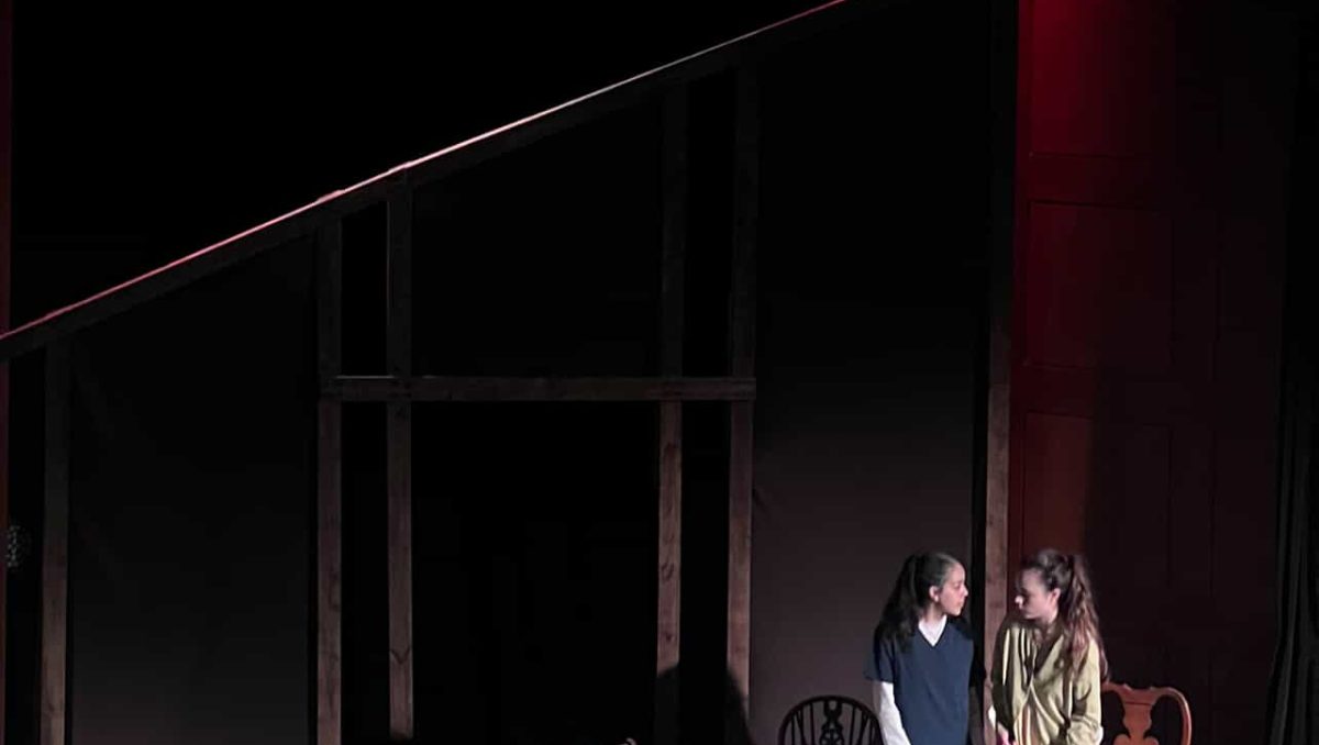 A student theatre set with two actors and a wooden structure which looks like a house.