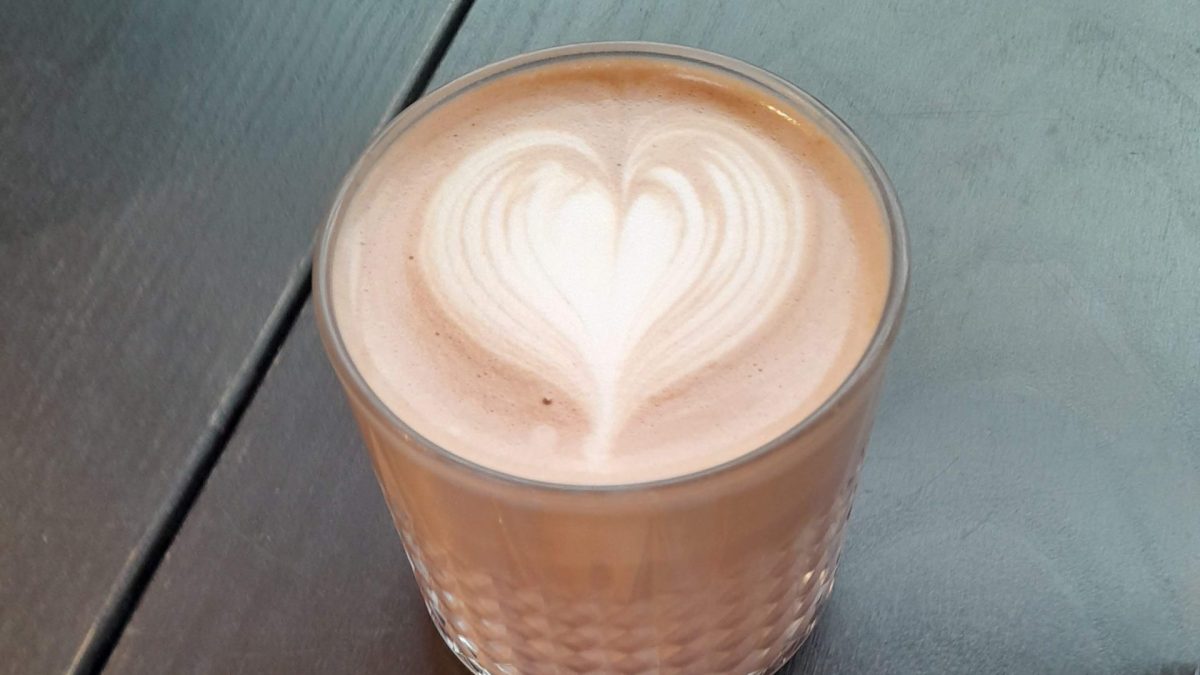 Hot chocolate with a love heart pattern on top, with a cookie by the side on a plate