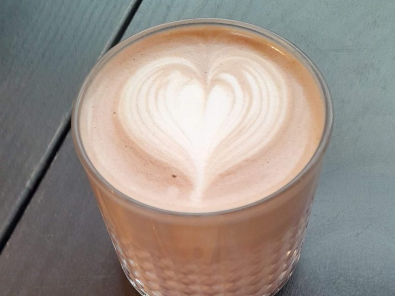 Hot chocolate with a love heart pattern on top, with a cookie by the side on a plate