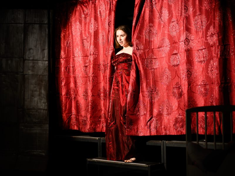 Lady Carla (Genevieve Kidd) pokes out from behind the curtain