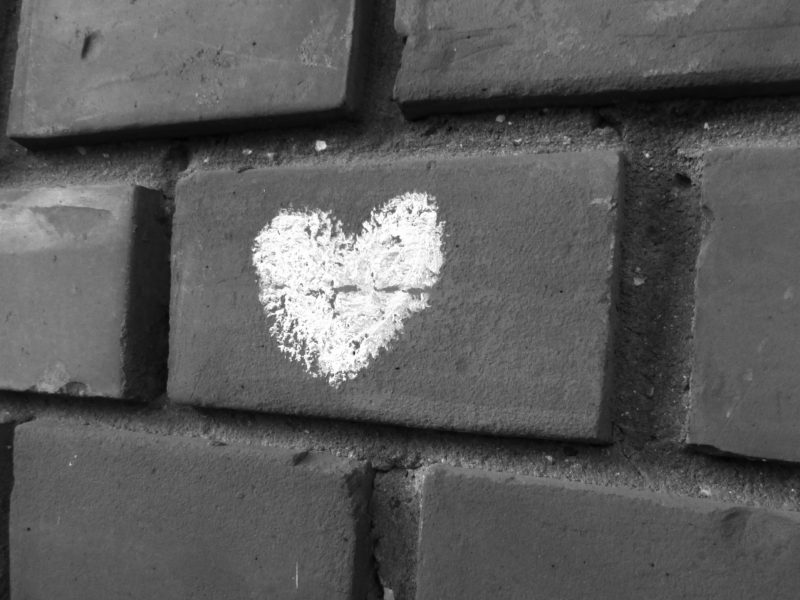 greyscale photo of a chalk love heart drawn on brick wall