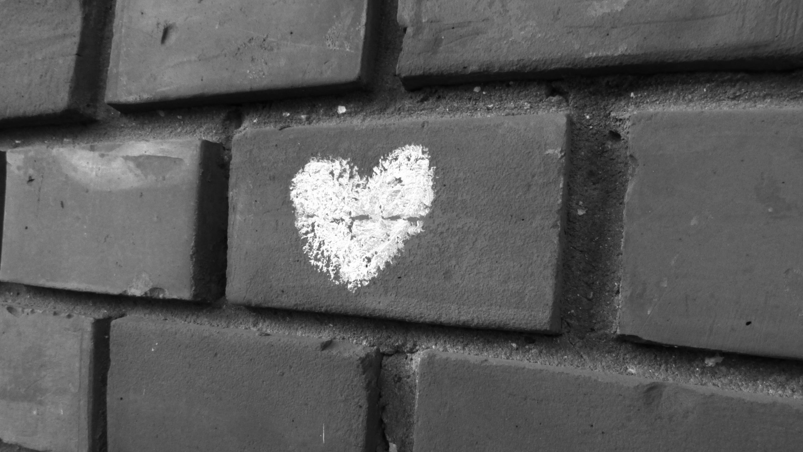 greyscale photo of a chalk love heart drawn on brick wall