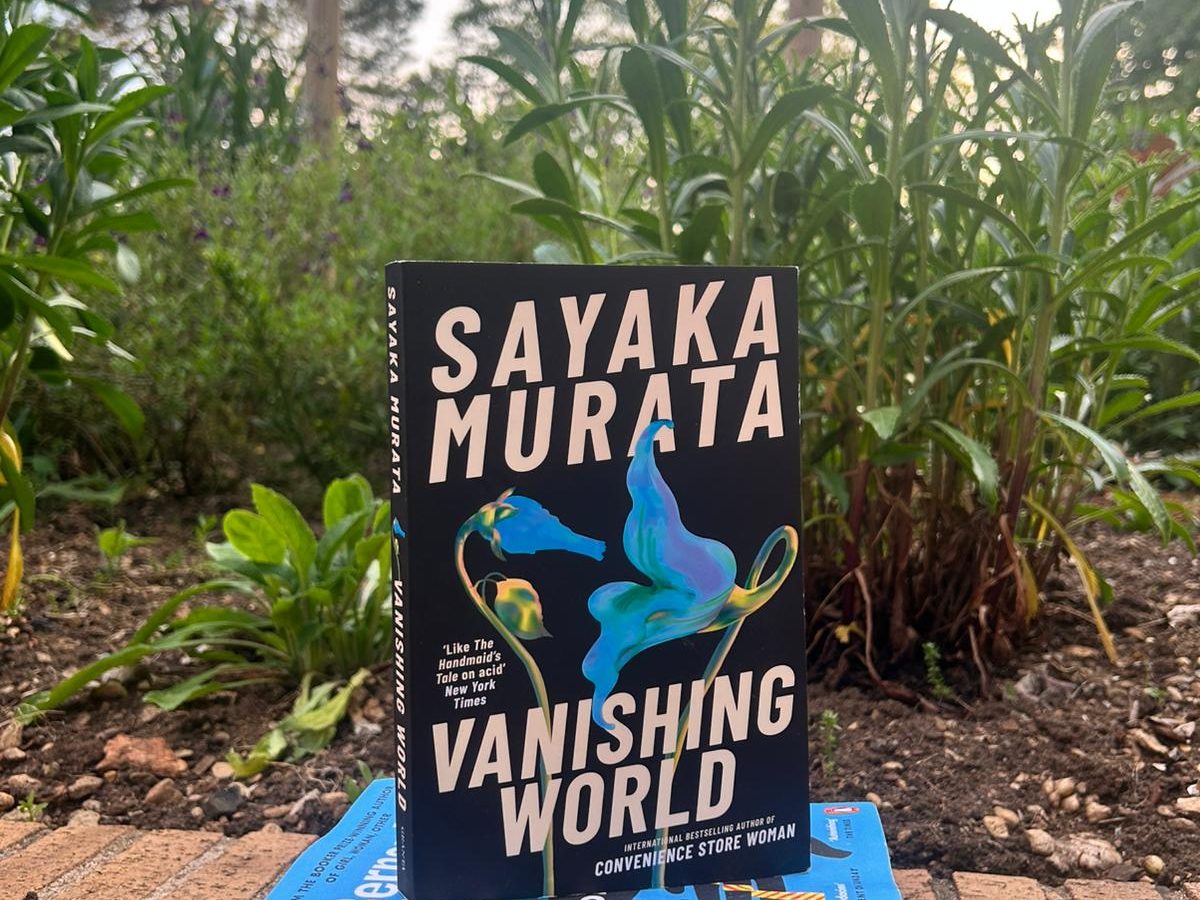 Three books in a pile in front of plants