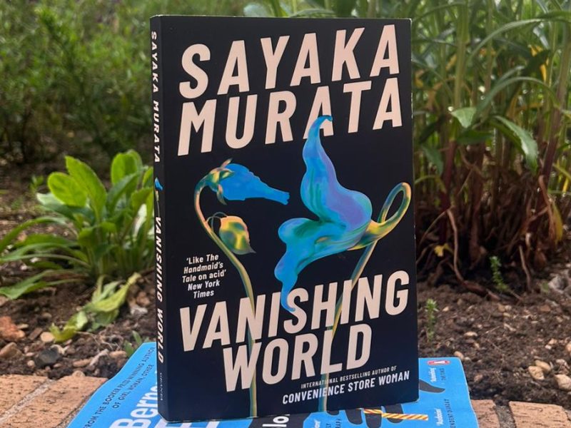 Three books in a pile in front of plants