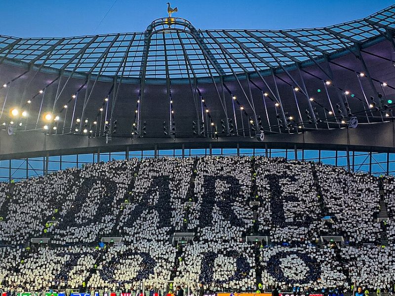 The Tottenham Hotspur Stadium, pictured in the evening. A card mosaic tifo reads "to dare is to do."
