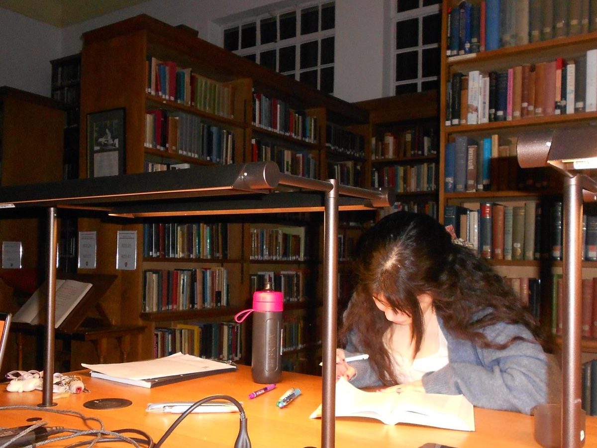 A woman annotating a book at a desk in a library.