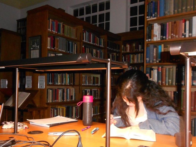 A woman annotating a book at a desk in a library.