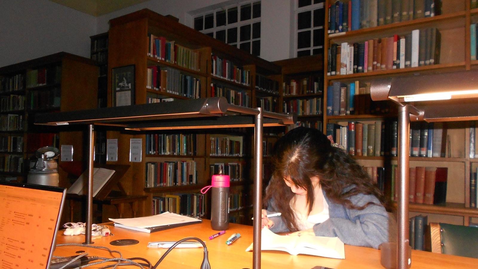 A woman annotating a book at a desk in a library.
