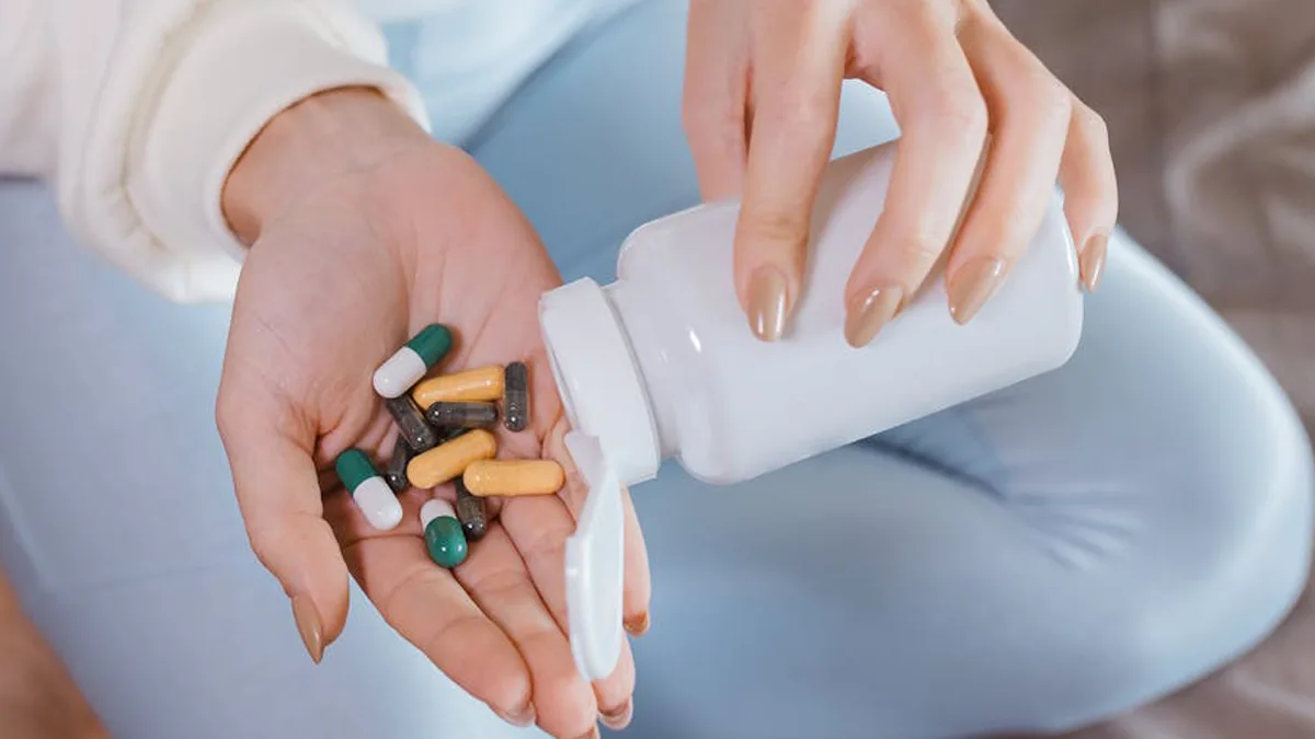 Close-up of hands pouring mixed capsules from a pill bottle indoors, focusing on healthcare and medicine
