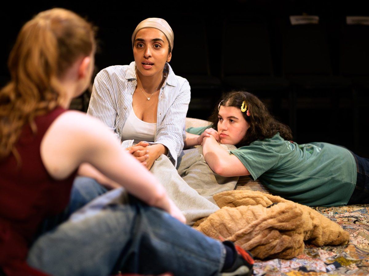 Three girls sit and talk on the floor.