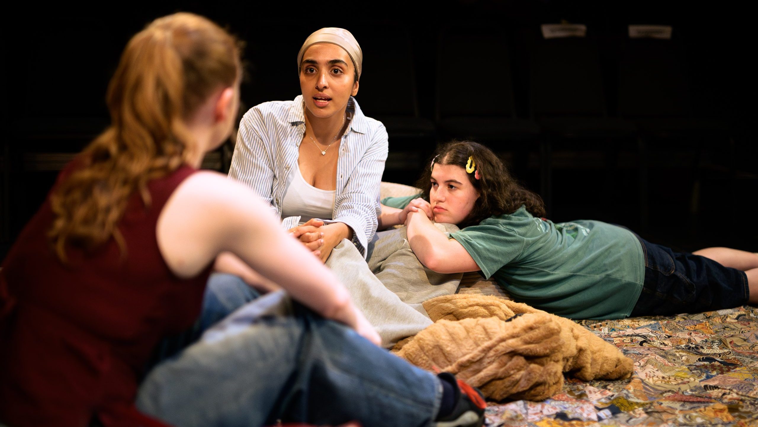 Three girls sit and talk on the floor.