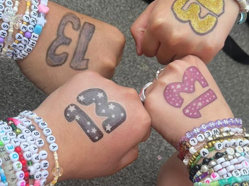 Taylor swift friendship bracelets on the arms of four friends with the number 13 painted on their hands.