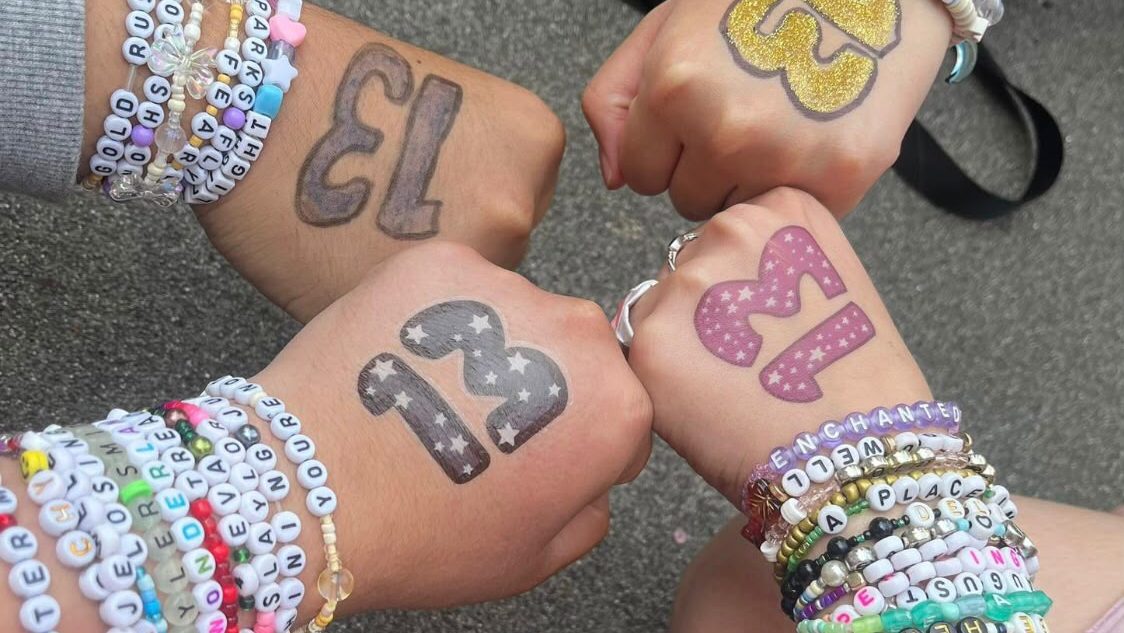 Taylor swift friendship bracelets on the arms of four friends with the number 13 painted on their hands.