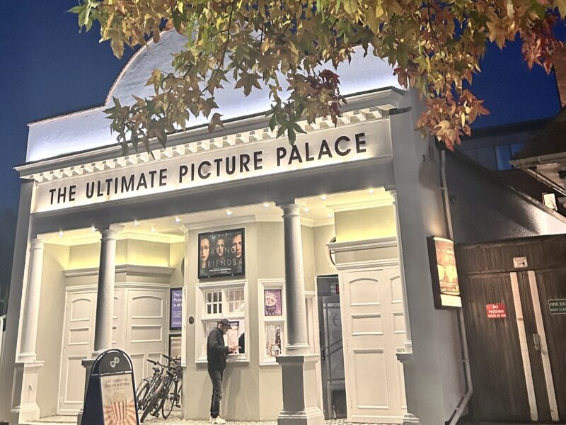 An image of films advertised at the Ultimate Picture Palace in Oxford, lit up, with a tree and leaves over the roof.
