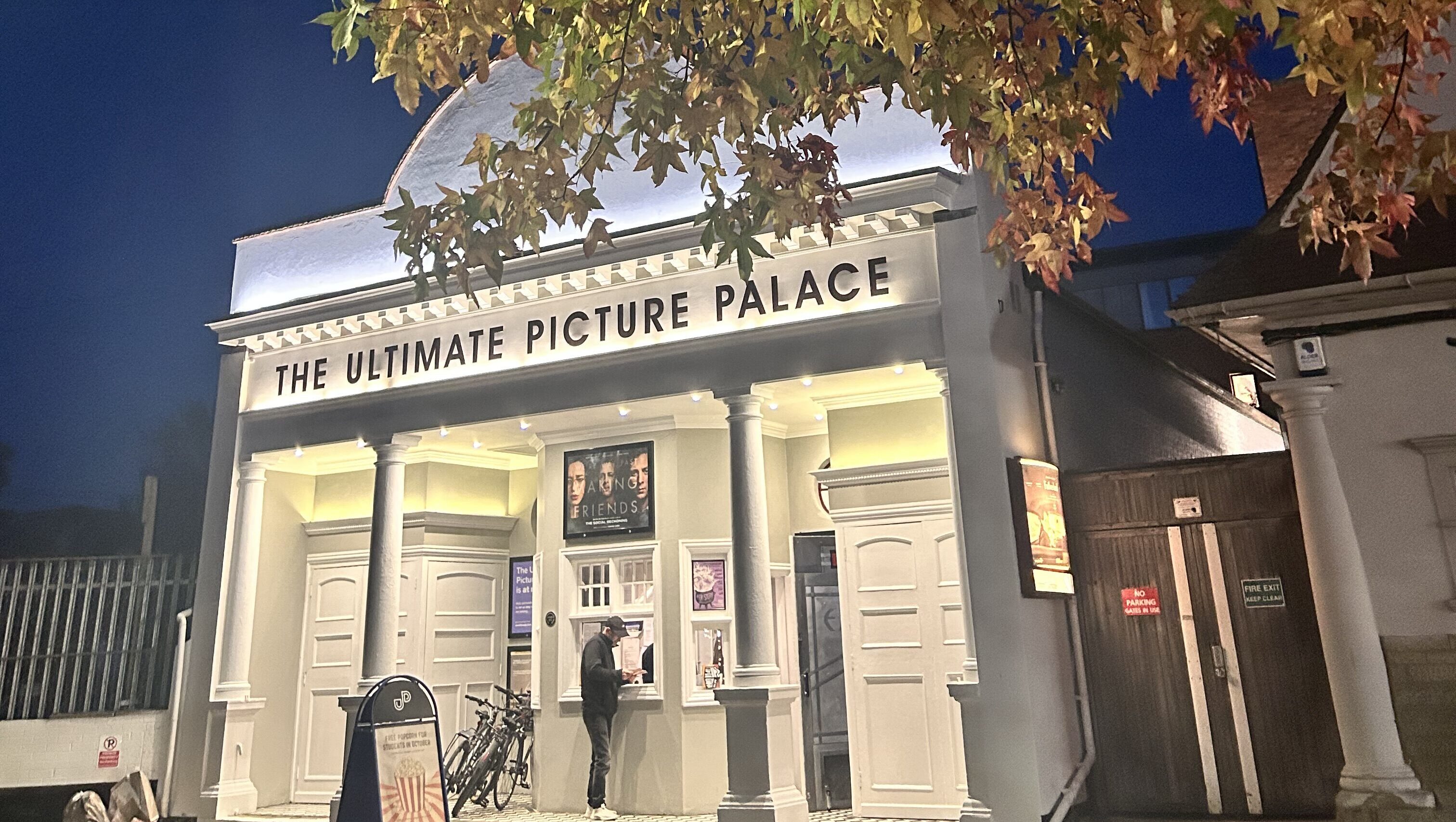 An image of films advertised at the Ultimate Picture Palace in Oxford, lit up, with a tree and leaves over the roof.