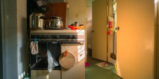 A messy kitchen. To the left is a stove with applicances on it. To the right is an open door leading into another room.
