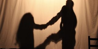 The silhouettes of a couple holding hands behind a white sheet